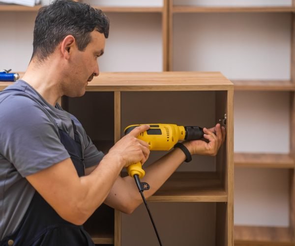Custom furniture production focused handyman attaching door fastener to wooden cabinet