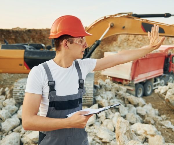 Management of project. Worker in professional uniform is on the borrow pit at daytime